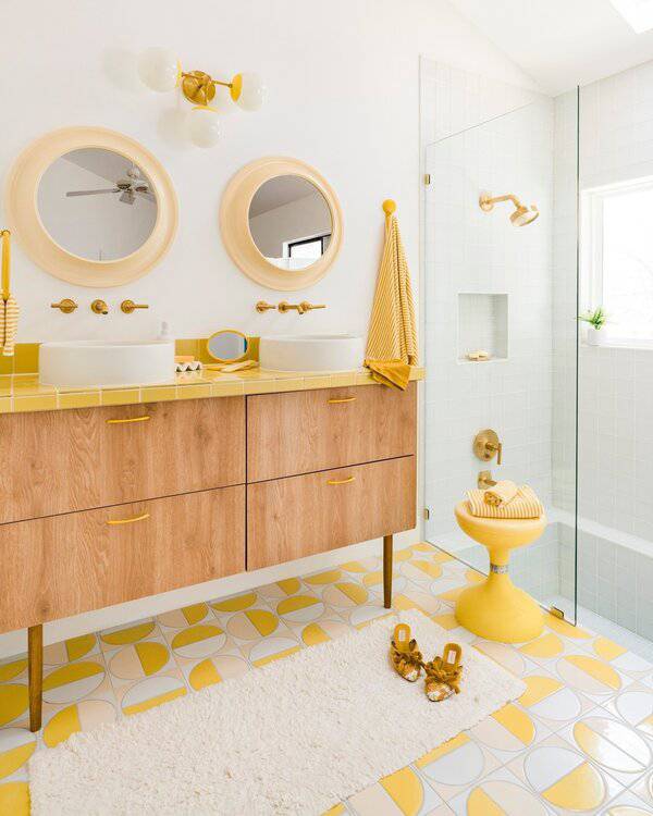 A bright bathroom with circular floor tiles, wood vanity topped with yellow tile, round mirrors, and brass fixtures for a cheerful look.
