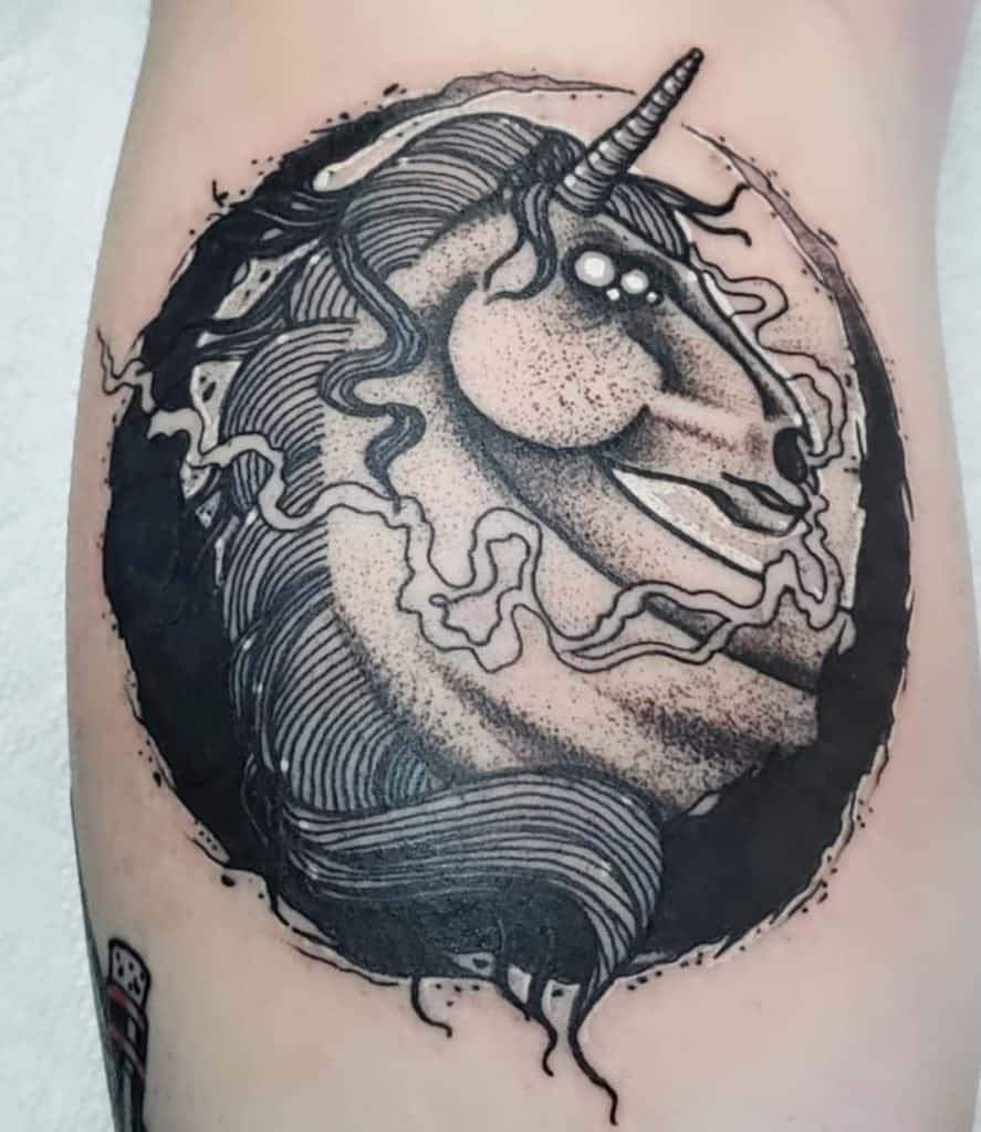Dark and surreal black ink tattoo of a unicorn with glowing eyes, surrounded by swirling smoke and a bold circular background.