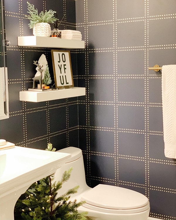Bathroom with white floating shelves, dark blue plaid wallpaper, and holiday decor accents.