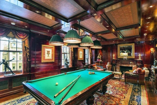 Luxurious billiard room with dark wood paneling, green felt table, and ornate ceiling design.