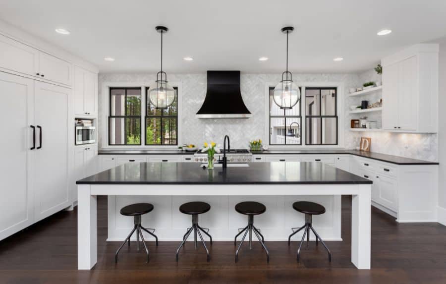 Classic kitchen with white cabinets, black countertops, large island, and pendant lighting.