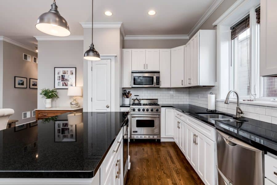 Classic kitchen with white cabinets, black countertops, pendant lights, and stainless steel appliances.
