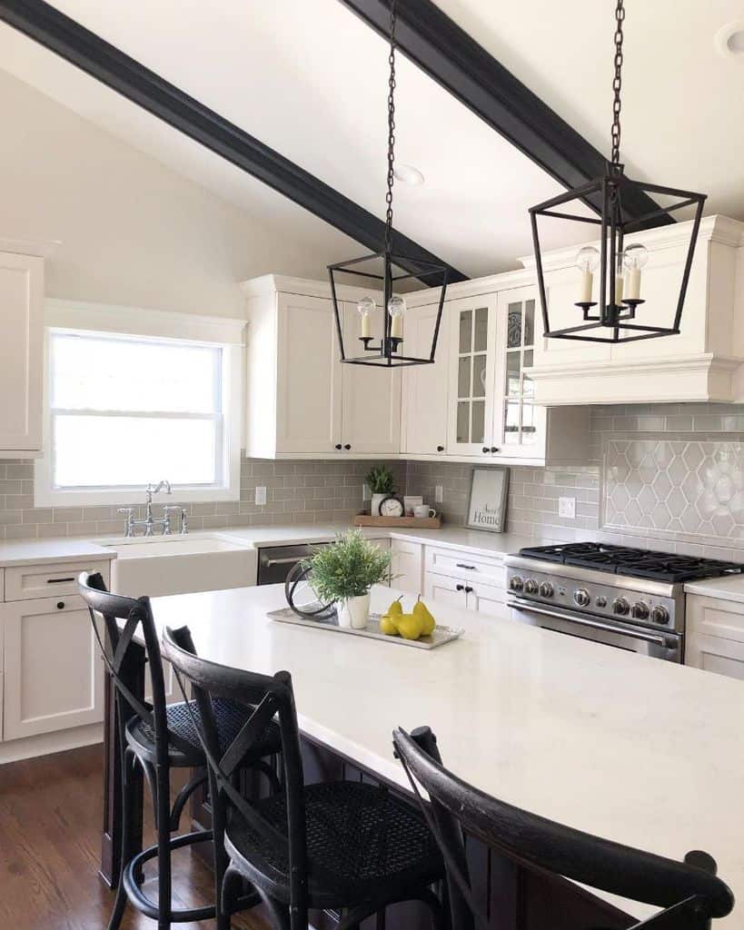 White kitchen with black beams, pendant lights, and a large island with chairs.