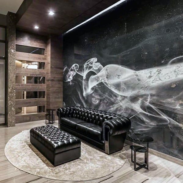 Black leather tufted sofa and ottoman in a modern room with a smoke-themed wall mural.
