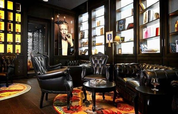 Luxurious dark wood library with leather chairs, colorful rugs, and bookshelves, portrait on the wall