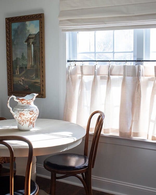 Classic dining room with half-length beige curtains, a vintage round table, and wooden chairs.