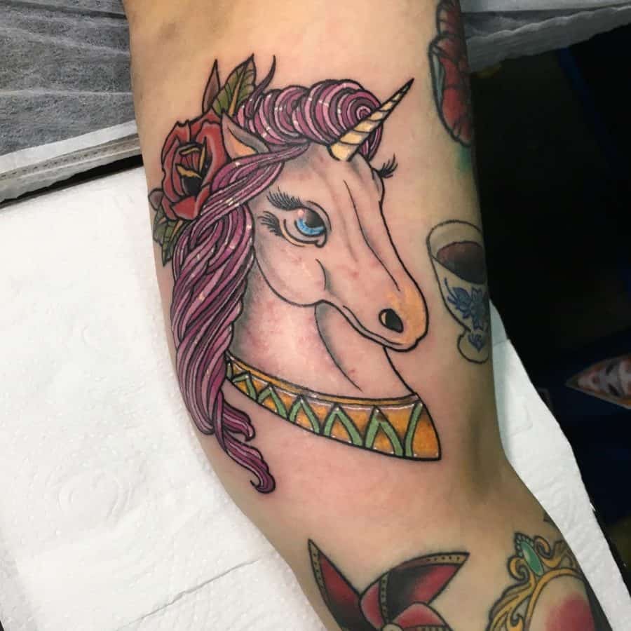 Colorful tattoo of a unicorn with flowing pink hair, adorned with roses and a golden collar, blending fantasy with a traditional tattoo style.