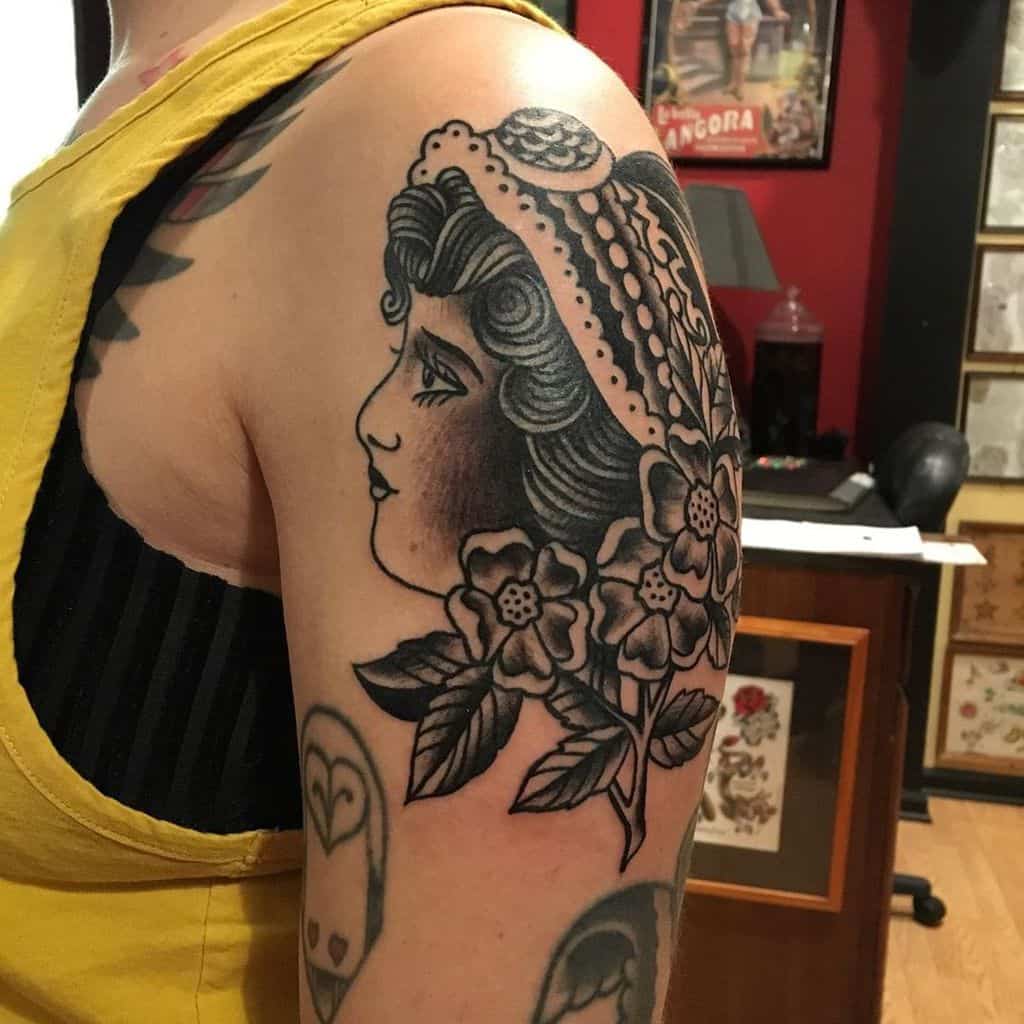 Traditional black and grey tattoo of a gypsy woman with a lace veil, floral details, and bold shading on the upper arm.