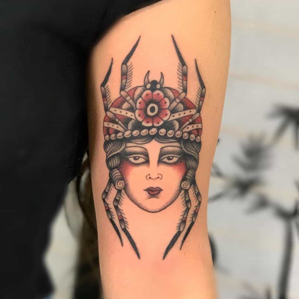 Unique tattoo of a mystical woman with a spider-themed headdress, bold shading, and intricate details on the upper arm.