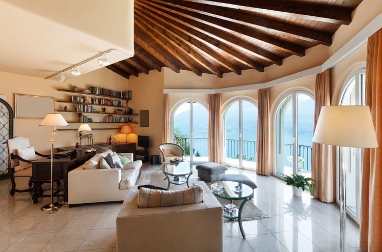 A classic-style, comfortable living room featuring a stunning beam ceiling, large arched windows offering panoramic views, and cozy furniture, creating a warm and inviting space