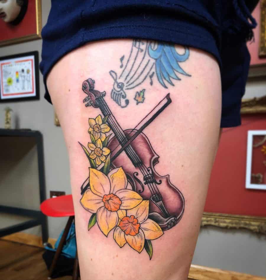 The tattoo features a violin intertwined with vibrant daffodils, creating a harmonious blend of music and nature.