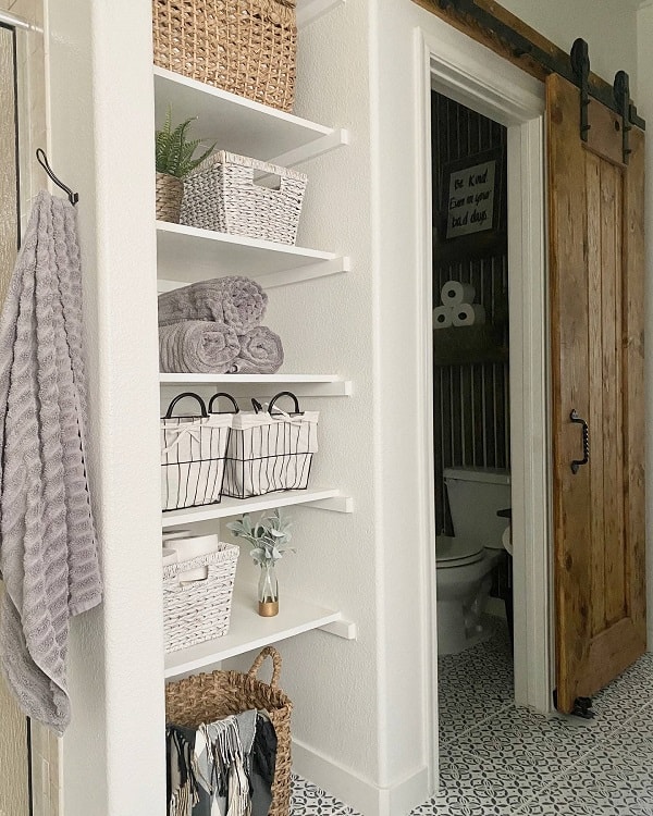 Natural wood sliding barn door leading to a bathroom with open shelving and patterned tile flooring.