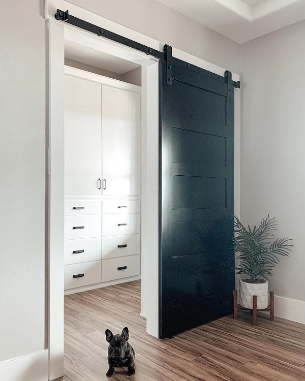 Black sliding barn door leading to a walk-in closet with white cabinetry in a modern bedroom.