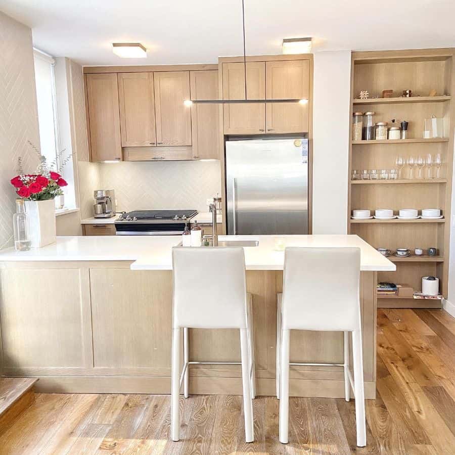 Elegant kitchen with light wood cabinets, white countertops, built-in shelves, and a modern minimalist pendant light.
