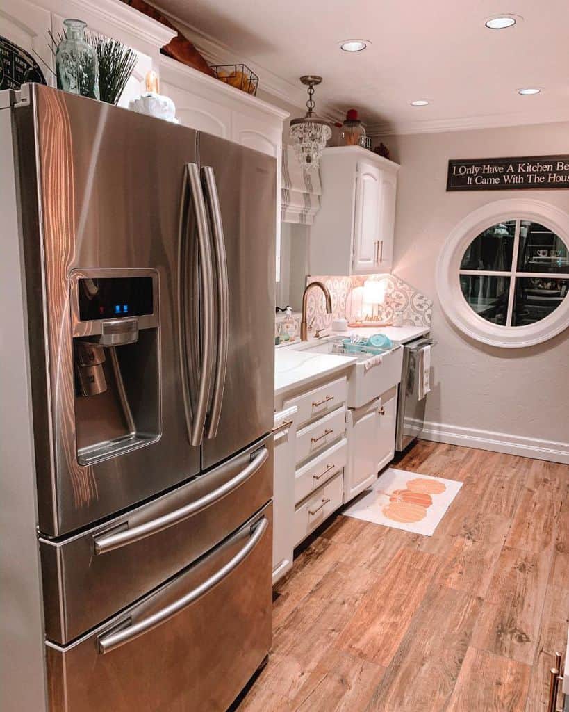 Charming farmhouse kitchen with white cabinetry, rustic wood flooring, and a round window centerpiece.