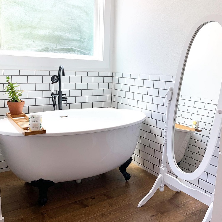 A modern bathroom with a white clawfoot bathtub, wooden floor, and a tall oval mirror
