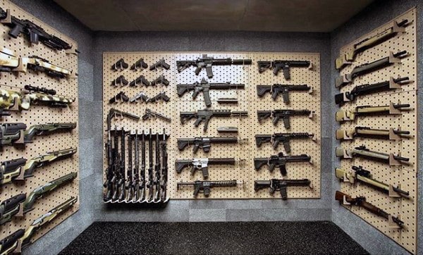 Organized gun room with pegboard walls displaying rifles, handguns, and firearm components.