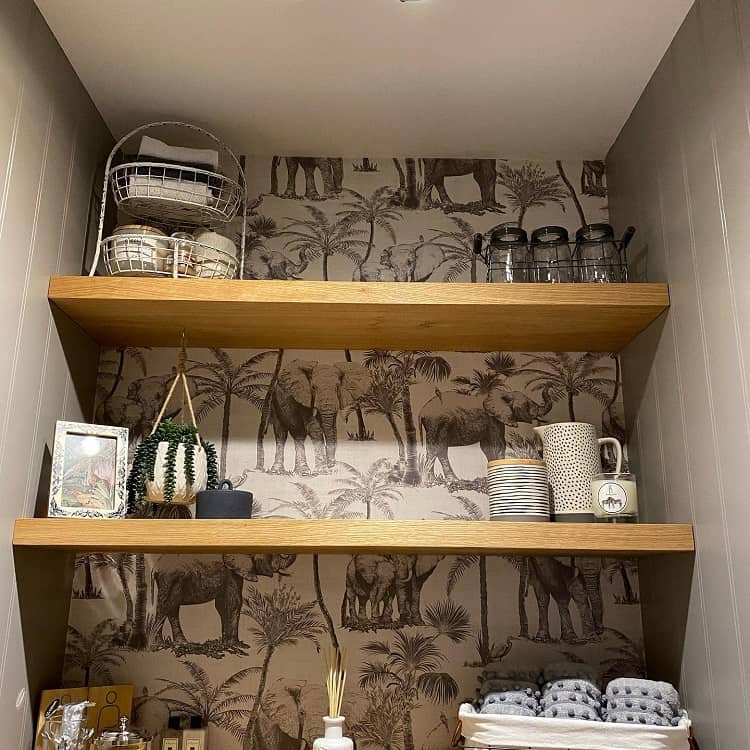 Wooden bathroom shelves with decor, storage baskets, and elephant-themed wallpaper backdrop.