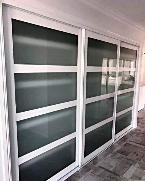 A modern sliding closet door design with white frames and frosted glass panels, offering a sleek and contemporary look