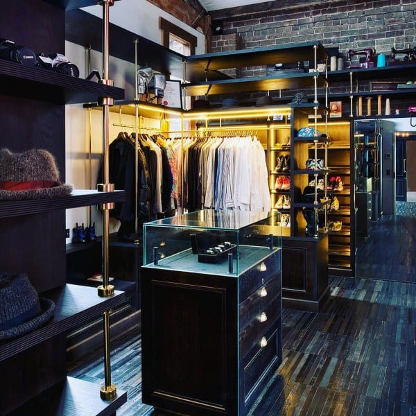 Industrial-style walk-in closet with brick walls, warm lighting, and dark wood shelving.
