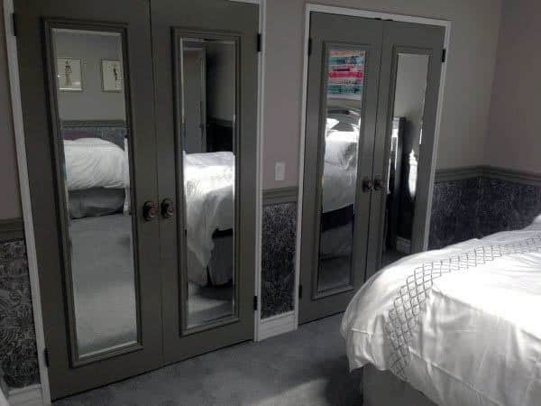 Bedroom with mirrored closet doors reflecting a cozy bed with white bedding and gray carpeted floor