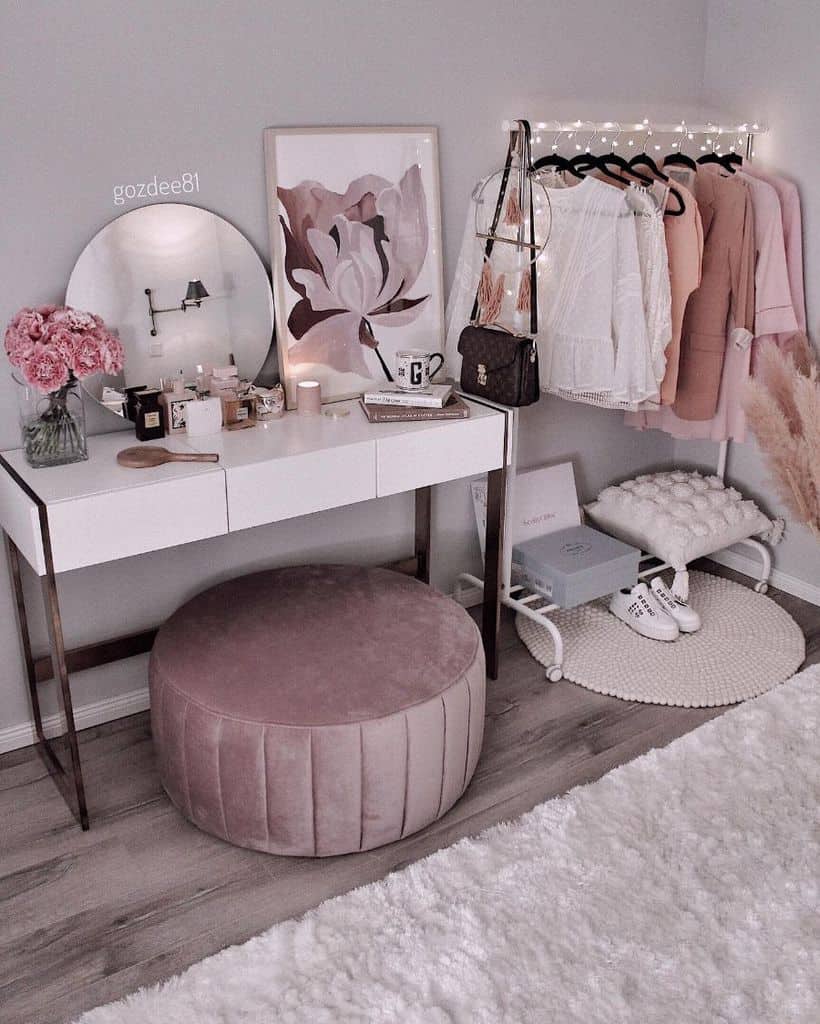 Feminine bedroom with vanity, pink ottoman, small clothes rack, and fairy lights.
