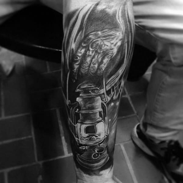 Black and grey tattoo of a miner's hand holding a lantern, detailed with deep shadows and dramatic lighting on the leg.