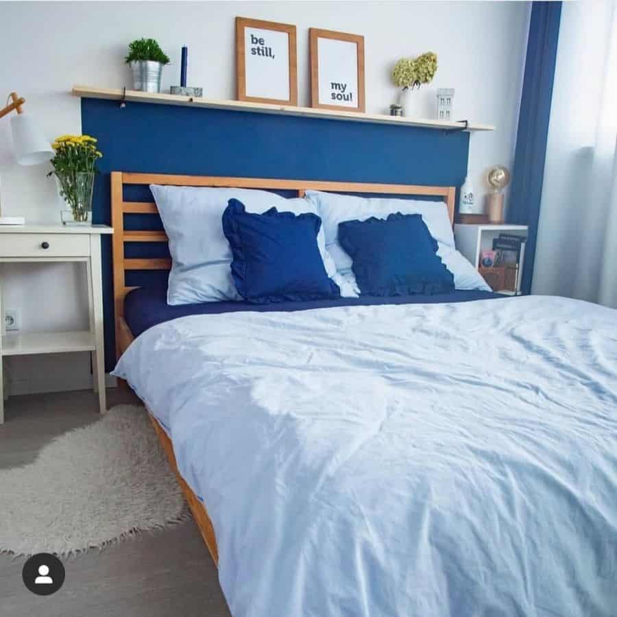 Cozy bedroom with blue accent wall, wooden bed frame, and navy blue pillows.