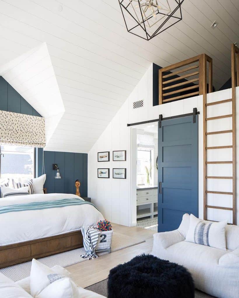 Bright coastal bedroom with vaulted ceiling, blue barn door, loft space, and wood accents.