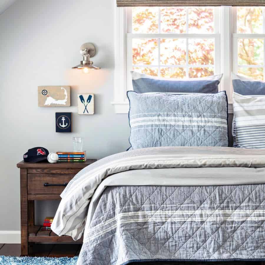 Coastal bedroom with blue quilted bedding, nautical wall art, and wooden nightstand.