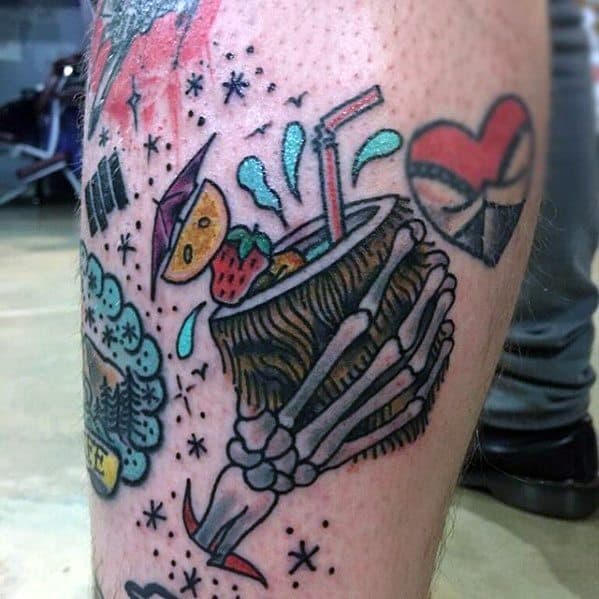 Bold and colorful tattoo of a skeleton hand holding a coconut drink with fruit garnish, straw, and umbrella on the lower leg.
