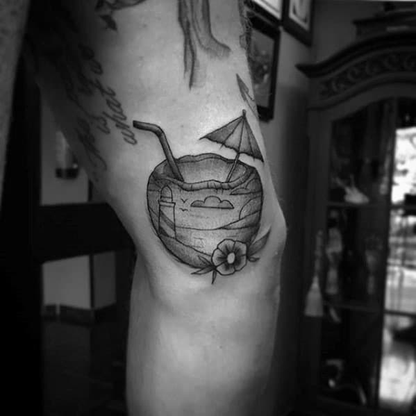 Black and grey coconut drink tattoo with umbrella, straw, beach scene, and flower detail, placed near the inner bicep.