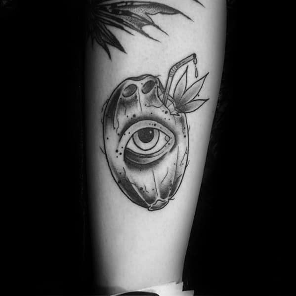 Surreal blackwork tattoo of a coconut with a realistic eye in the center, straw, and leaves, placed on the lower leg.