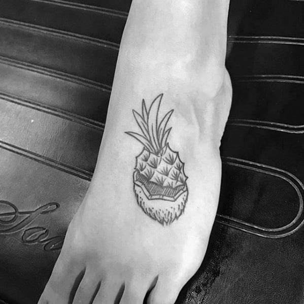 Small black line tattoo of a coconut and pineapple hybrid fruit design, inked on the top of the foot.