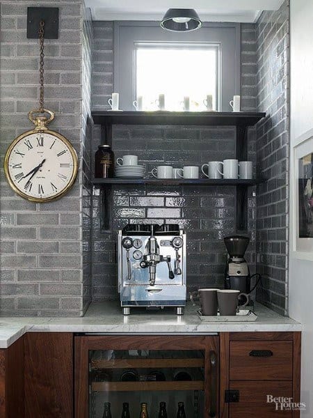 Industrial coffee bar with grey brick backsplash, espresso machine, wooden shelves, and clock.