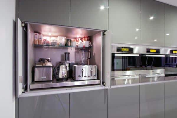 Modern hidden coffee bar with grey cabinets, built-in appliances, and illuminated storage space.