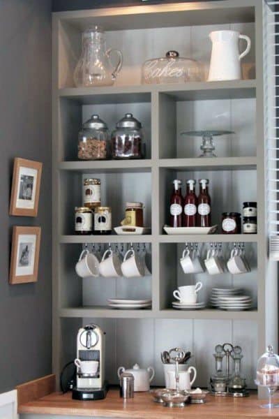Rustic coffee bar with open shelves, wooden countertop, mugs, jars, and espresso machine.