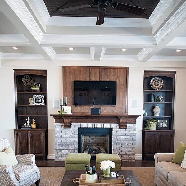 A living room with a coffered ceiling, crown molding, built-in bookshelves, a fireplace, and modern lighting, creating a cozy yet sophisticated ambiance