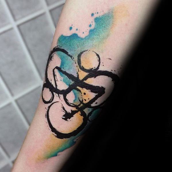 Coheed and Cambria Keywork tattoo with black ink lines and watercolor splashes of teal and orange for a bold, artistic contrast.