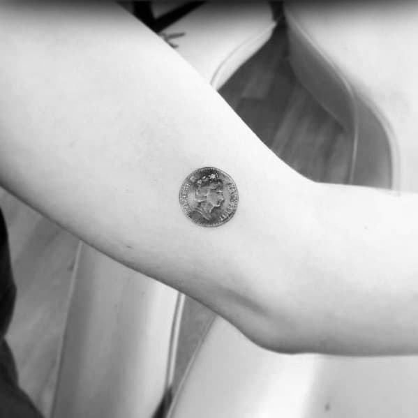 Small, detailed coin tattoo on the inner arm, featuring fine shading to create a realistic miniature currency design.