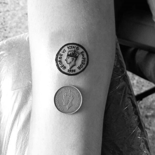 Realistic tattoo of a 1938 King George VI coin on the forearm, placed beside an actual coin for a detailed comparison.