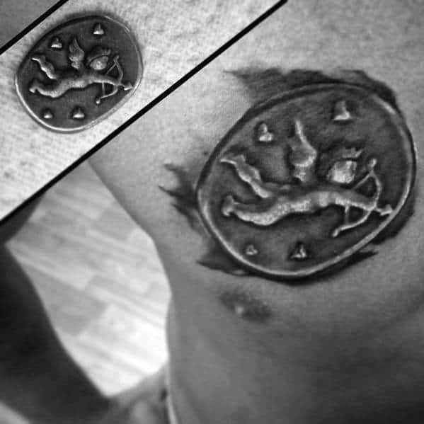 Realistic tattoo of a coin featuring Cupid with a bow, surrounded by hearts, designed with a 3D effect and torn-skin detail on the chest.