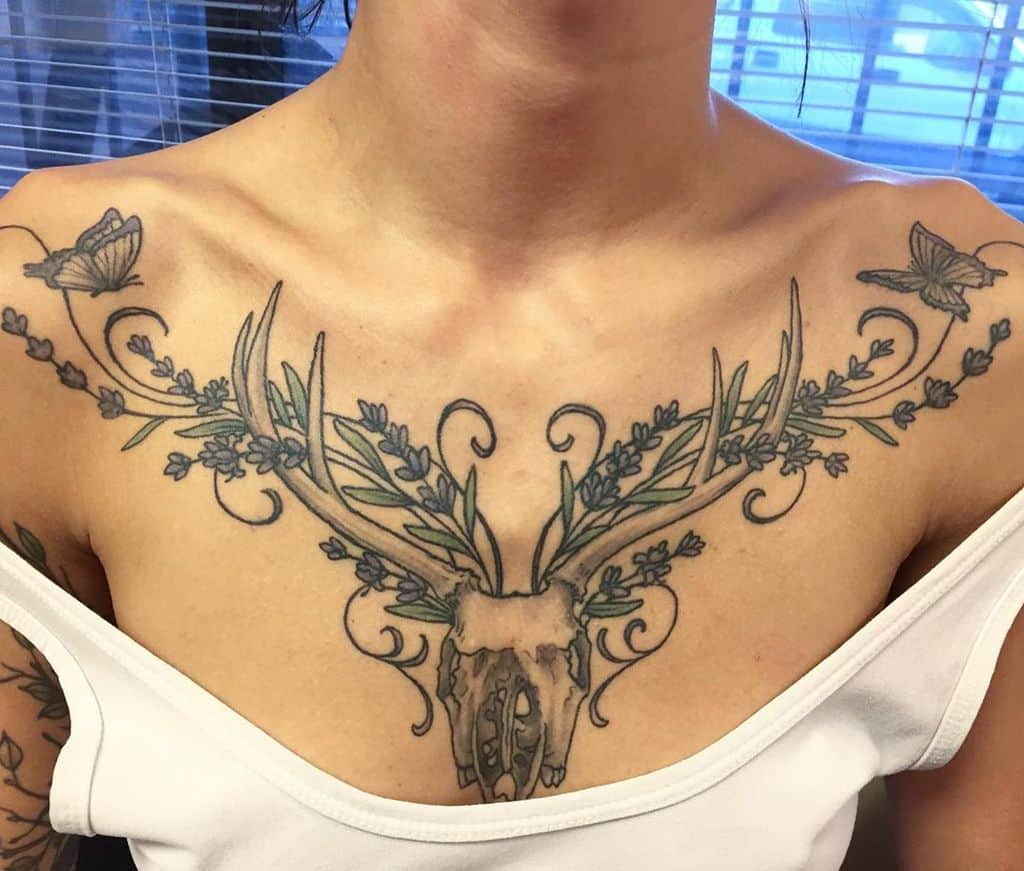 A detailed chest tattoo featuring a deer skull with antlers adorned with lavender and butterfly accents, extending across the collarbones.