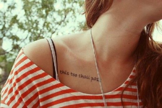 A "This Too Shall Pass" tattoo in cursive on the collarbone area of a person's shoulder.