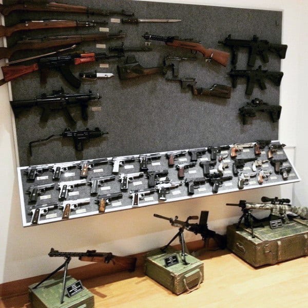 A collector's armory display featuring rifles, pistols, and machine guns, neatly arranged on walls and stands with labeled plaques.