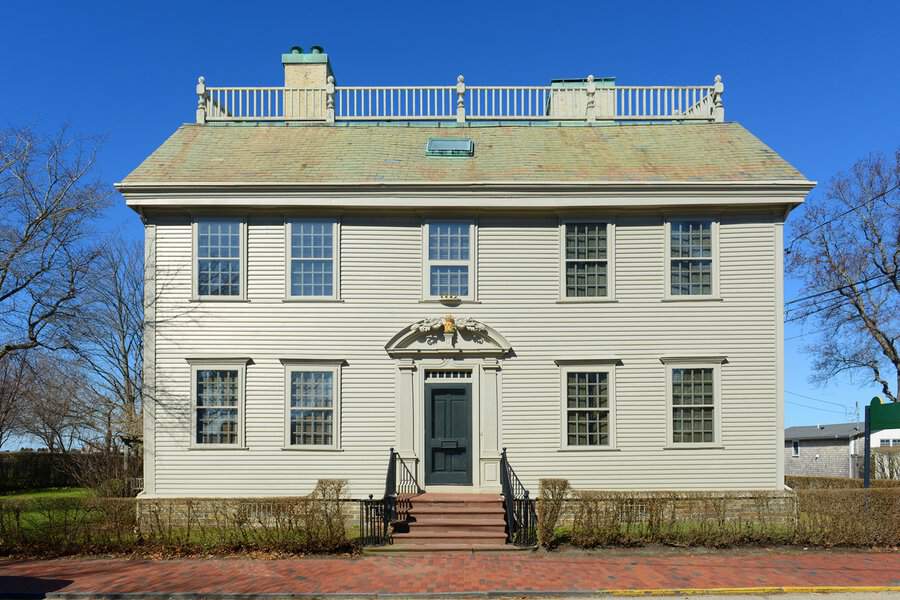 Symmetrical colonial Georgian house with multi-paned windows, a decorative pediment, and clapboard siding in pale neutral tones.