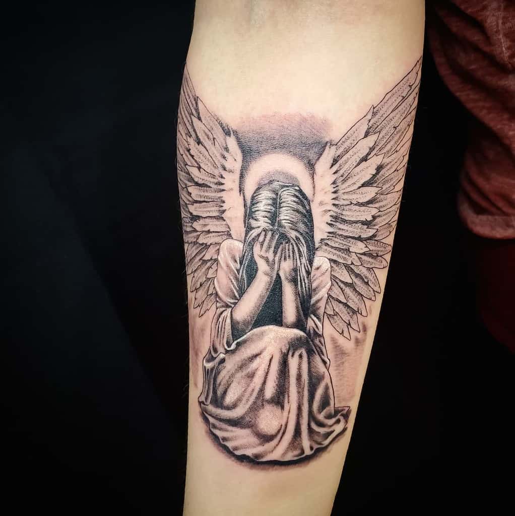 Tattoo of a winged angel sitting with head in hands with halo above
