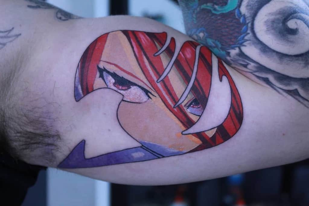 Colorful tattoo of Erza Scarlet’s intense gaze inside the Fairy Tail guild emblem, featuring bold shading and vibrant red tones on the inner arm.