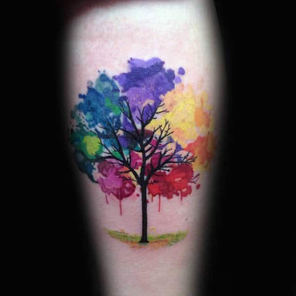 Tattoo of a tree with bare branches and colorful splashes as leaves on an arm