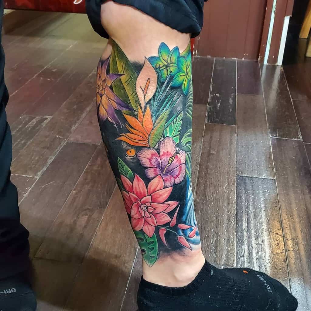 A colorful leg sleeve tattoo featuring vibrant flowers and leaves in various shades with yellow eyes peaking